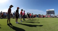Junior golfers at a tournament with scoreboard in the background.