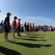 Junior golfers at a tournament with scoreboard in the background.